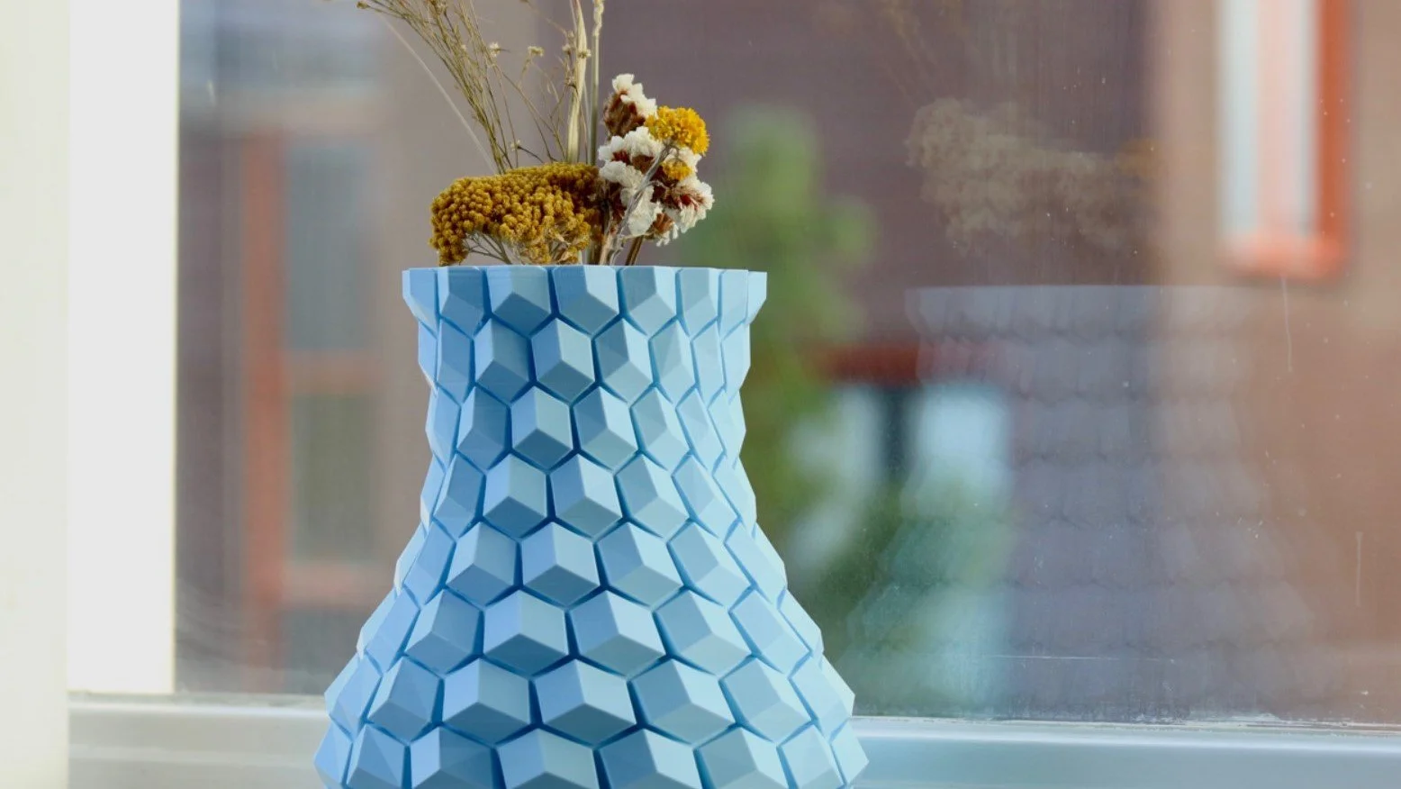 3D-printet geometrisk blå vase med tørrede blomster i vindueskarm